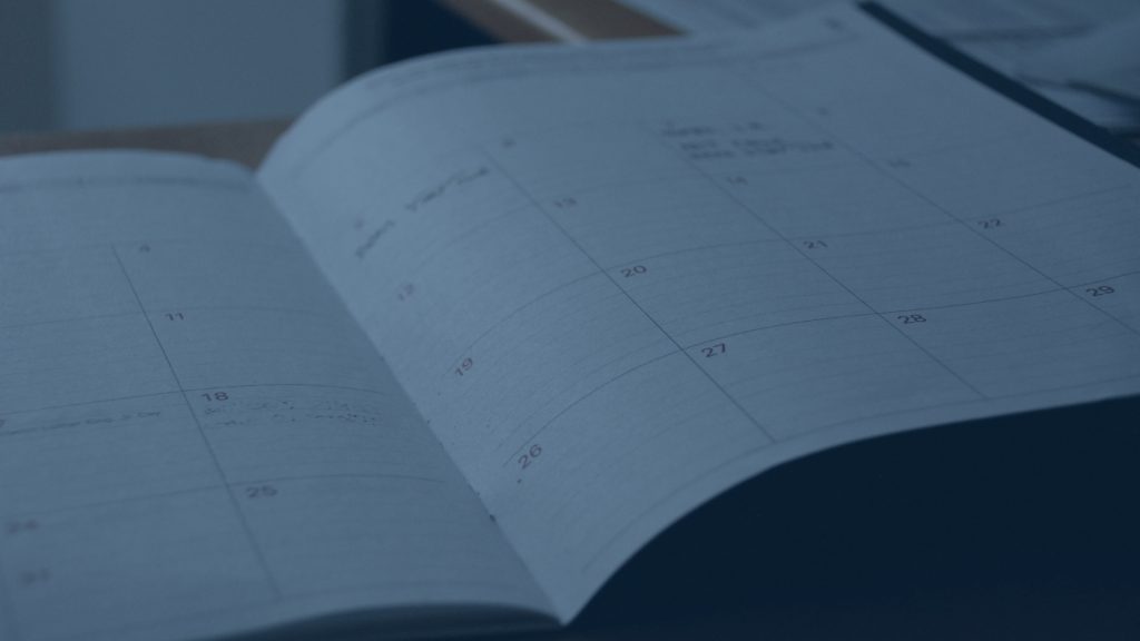 Close-up of an open paper planner showing calendar pages with dates, presented with a cool blue color overlay.