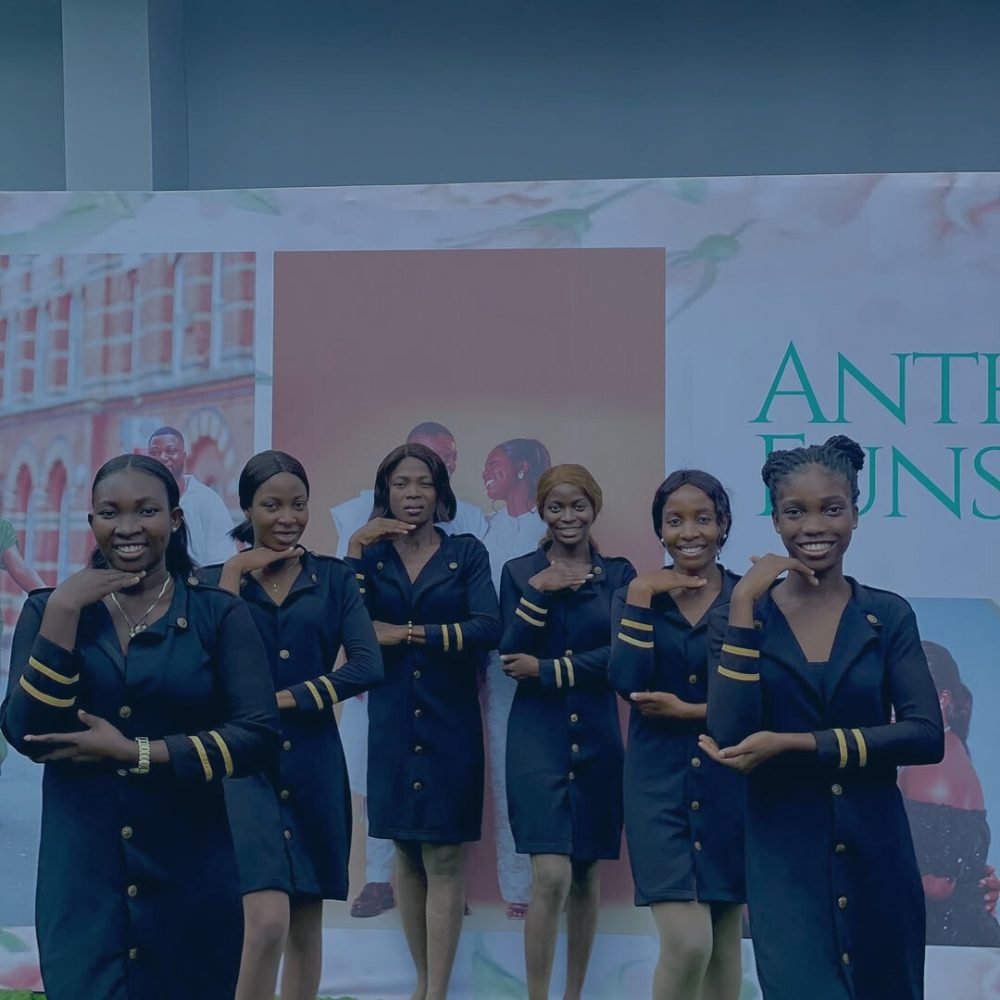 Mastering Body Language - Group of six female event ushers smiling in matching black dresses with gold sleeve stripes, posing together in front of an event backdrop.